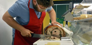 Matteo Grossi, who helped begin Famiglia Grossi Artisti Salumieri, cuts fresh slices of ham for a customer’s sandwich in the lunch hours. In With the Old, In With the New