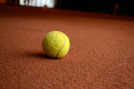 Tennis balls skid and collect dust from the red clay surface of the court.