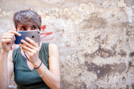 Photographer Samantha Gazzetta peeks behind her iPhone outside her shop in Cagli. Photo by Aimee Elber / Gonzaga in Cagli